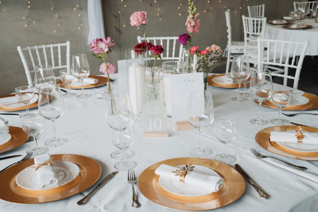 Runder Tisch mit goldenen Platztellern, Kerzen und Blumen